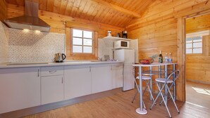 A wooden cabin kitchen with a microwave, refrigerator, and a small dining table with chairs. - Holiday home La Cabañita de Javi with Sea View, Garden & Wi-Fi (Tuineje)