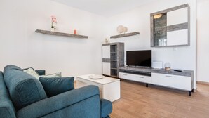Un soggiorno moderno con divano, tavolino, televisione e angolo cottura con piano di lavoro e pensili.