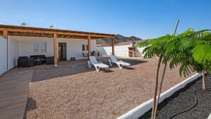 Un'area esterna coperta con due poltrone bianche, un pergolato in legno e un patio lastricato di ghiaia.