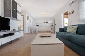 A modern living room with a TV, a sofa, a coffee table, and a kitchen in the background. - Holiday Home 'Vista Paraiso' with Mountain View, Garden & Wi-Fi (Tuineje)