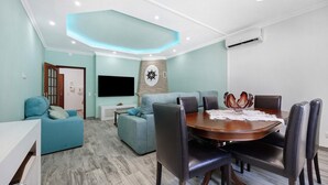 A modern living room with a dining area, teal sofas, a wooden dining table, and a mounted TV. - Apartment Casa Violeta with Terrace, A/C & Wi-Fi (Lagos)