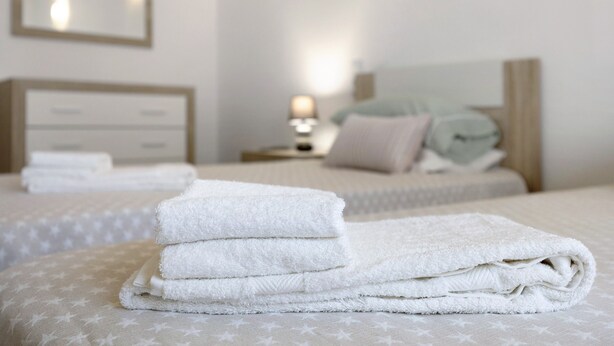 A neatly made bed with a white comforter and pillows, a bedside table with a lamp, and a wall-mounted mirror. - Apartment Casa Violeta with Terrace, A/C & Wi-Fi (Lagos)