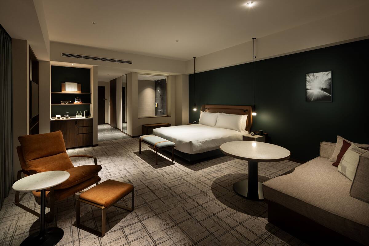 A hotel room with a bed, a sofa, a chair, a small table, and a desk with a lamp.