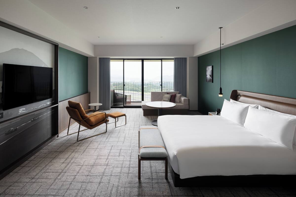 A hotel room with a large bed, a TV, a seating area with a table and chairs, and a balcony with a view.