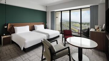 Habitación de hotel con dos camas, un escritorio, una silla y un balcón con vistas.