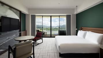 Une chambre d’hôtel avec un lit, une télévision, une chaise, une petite table et une grande fenêtre donnant sur le paysage.