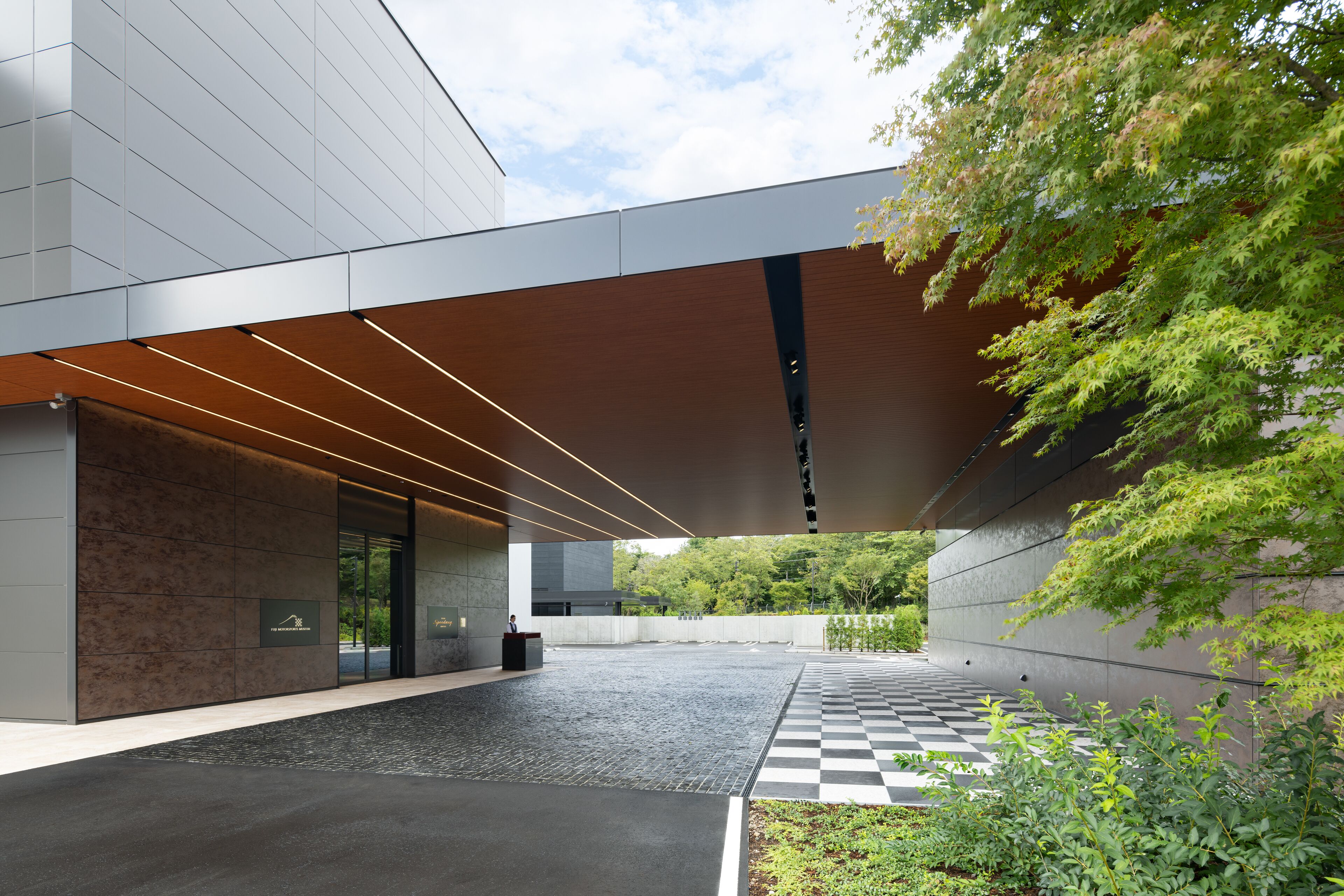 Un bâtiment moderne doté d’un sol à motifs en damier, d’une entrée couverte et d’un espace jardin agrémenté d’arbres.