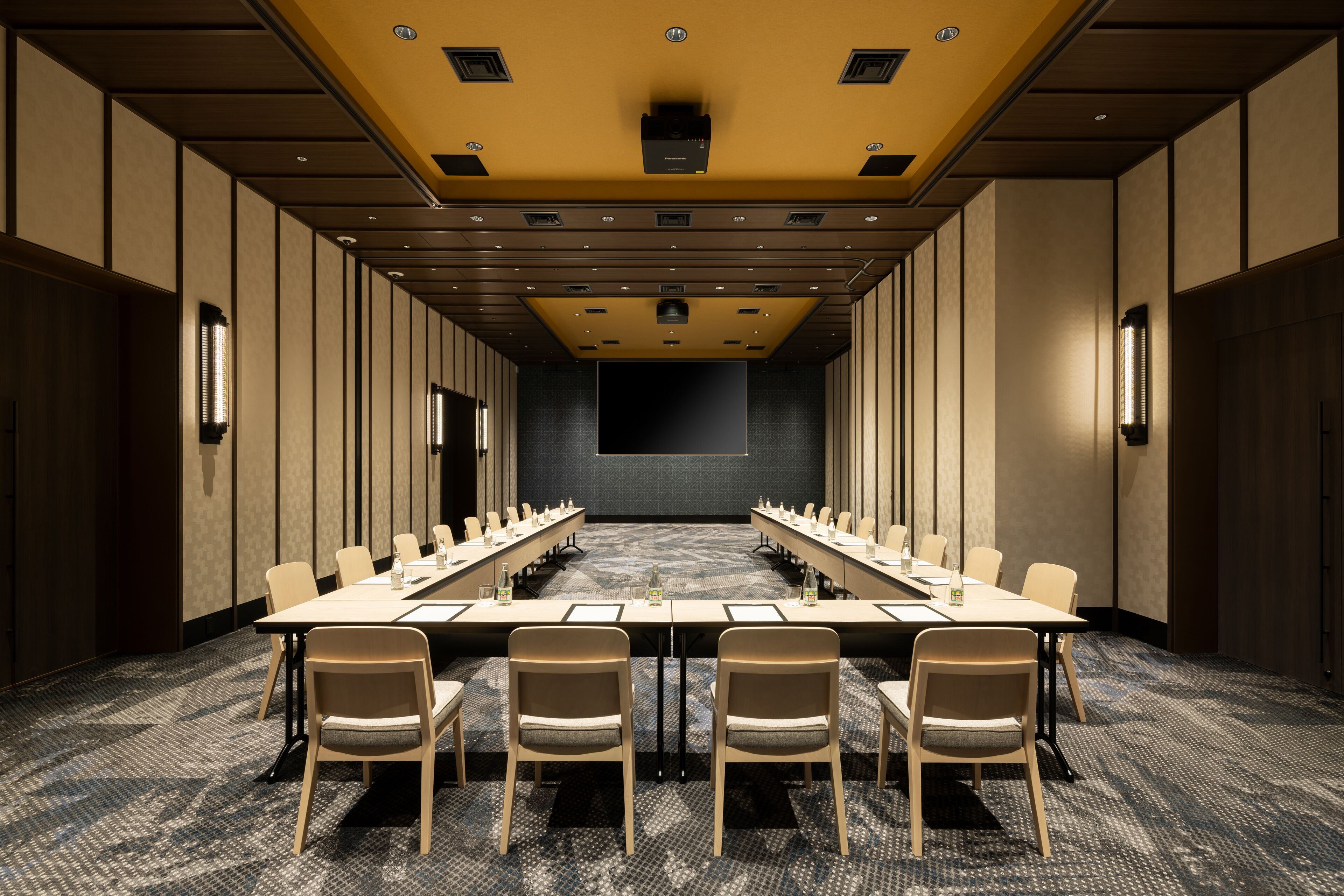 Una sala de conferencias con una larga mesa, sillas y una pantalla grande al frente.
