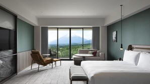 Une chambre d’hôtel avec un lit, un canapé, une petite table, une chaise et une vue sur une montagne.