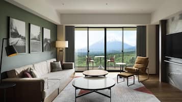 A modern hotel room with a sofa, a round coffee table, a TV, and a balcony with a mountain view.