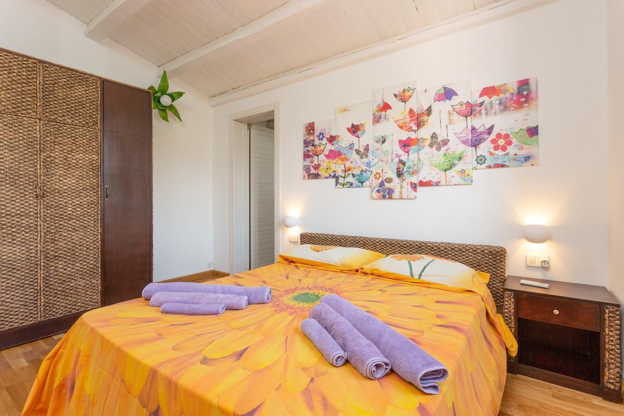Een slaapkamer met een bed, een groot bloemistisch kunstwerk aan de muur en een geweven scheidingswand.