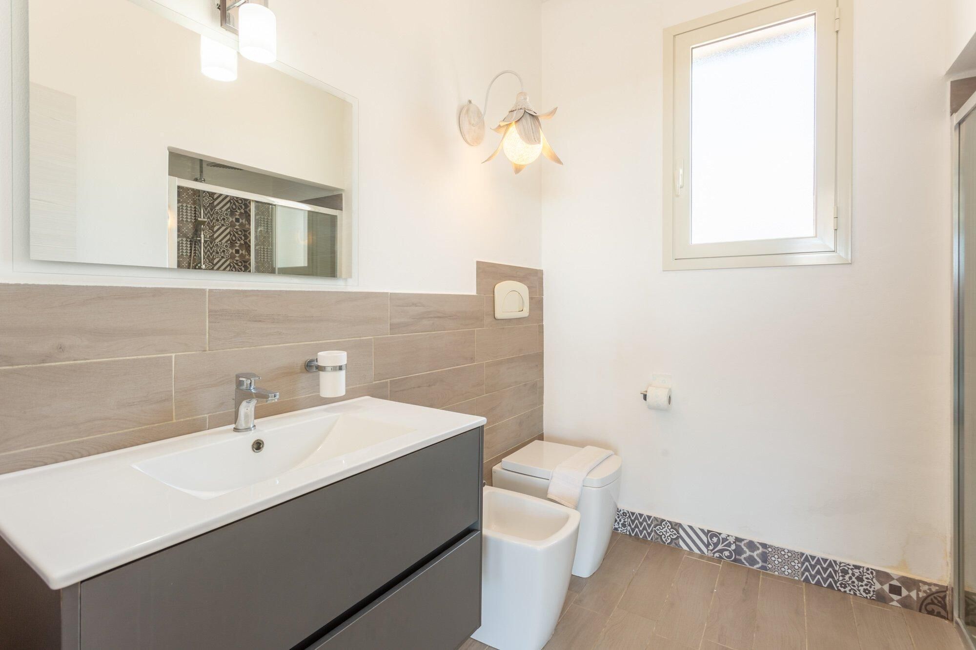 A modern bathroom with a large mirror, a sink, a toilet, and a shower.