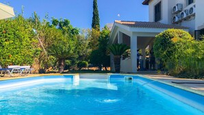 A swimming pool with clear blue water, surrounded by lush greenery and a building with a tiled roof. - Villa Iliana in Poli Crysochous (Polis)