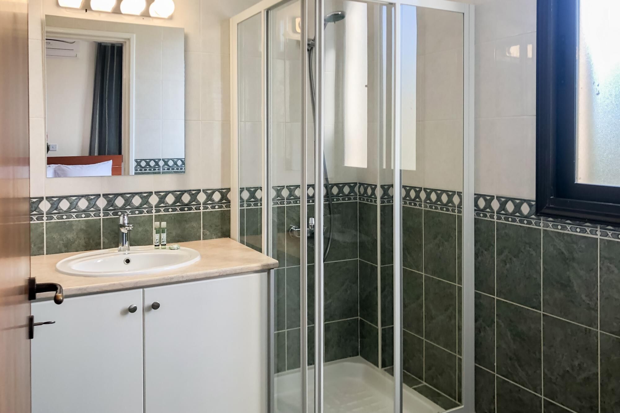 Ein Badezimmer mit einer gläsernen Duschkabine, einem Waschbecken mit Spiegel darüber und dekorativen Fliesenbordüren.