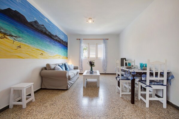 A living room with a painting, a sofa, a coffee table, and a dining area with chairs and a table.