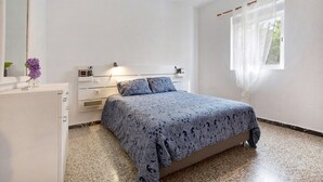 Un dormitorio con cama, cómoda, mesita de noche, ventana con cortinas y espejo.