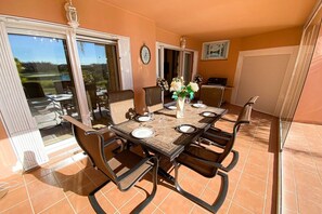 Un coin repas avec une table dressée pour quatre personnes, des chaises, un vase rempli de fleurs et une vue à travers des portes vitrées.