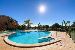Une piscine à bord incurvé, entourée de palmiers et d’un bâtiment.