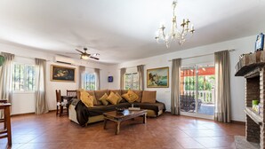 A spacious living room with a sofa, a coffee table, a fireplace, and a balcony with a view. - Holiday Home "Casa Mis Nietos" with Pool, Garden and Wi-Fi (Monda)