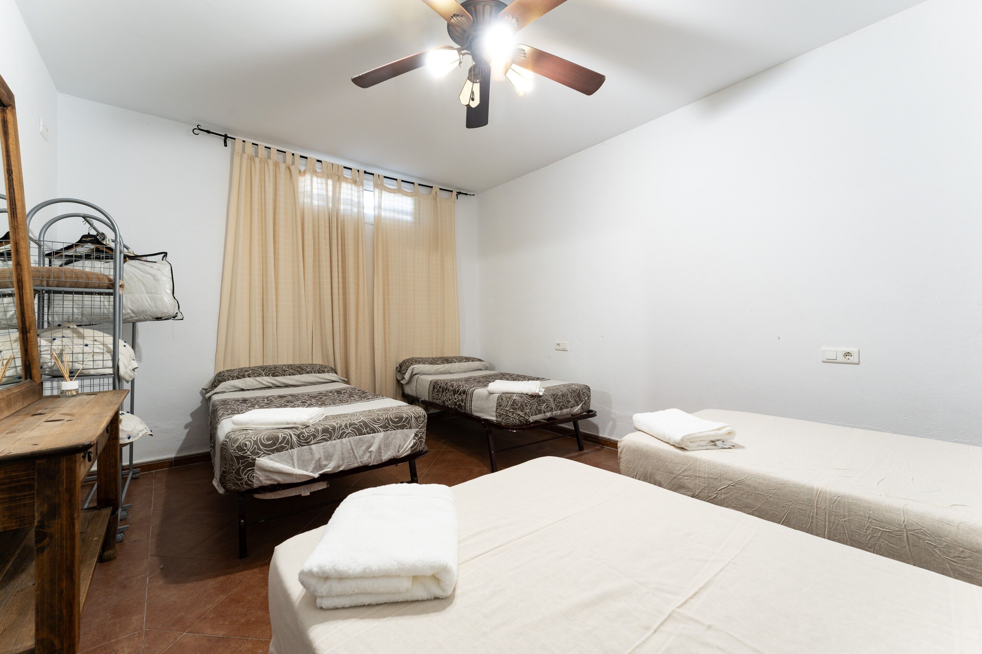 A hotel room with two beds, a wooden dresser, a ceiling fan, and a window with curtains.