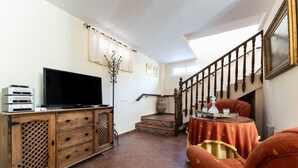 A living room with a TV, wooden cabinet, staircase, and a table with a vase. - Holiday Home "Casa Mis Nietos" with Pool, Garden and Wi-Fi (Monda)