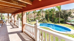 A covered outdoor area with a pool, lounge chairs, and a view of palm trees and hills. - Holiday Home "Casa Mis Nietos" with Pool, Garden and Wi-Fi (Monda)