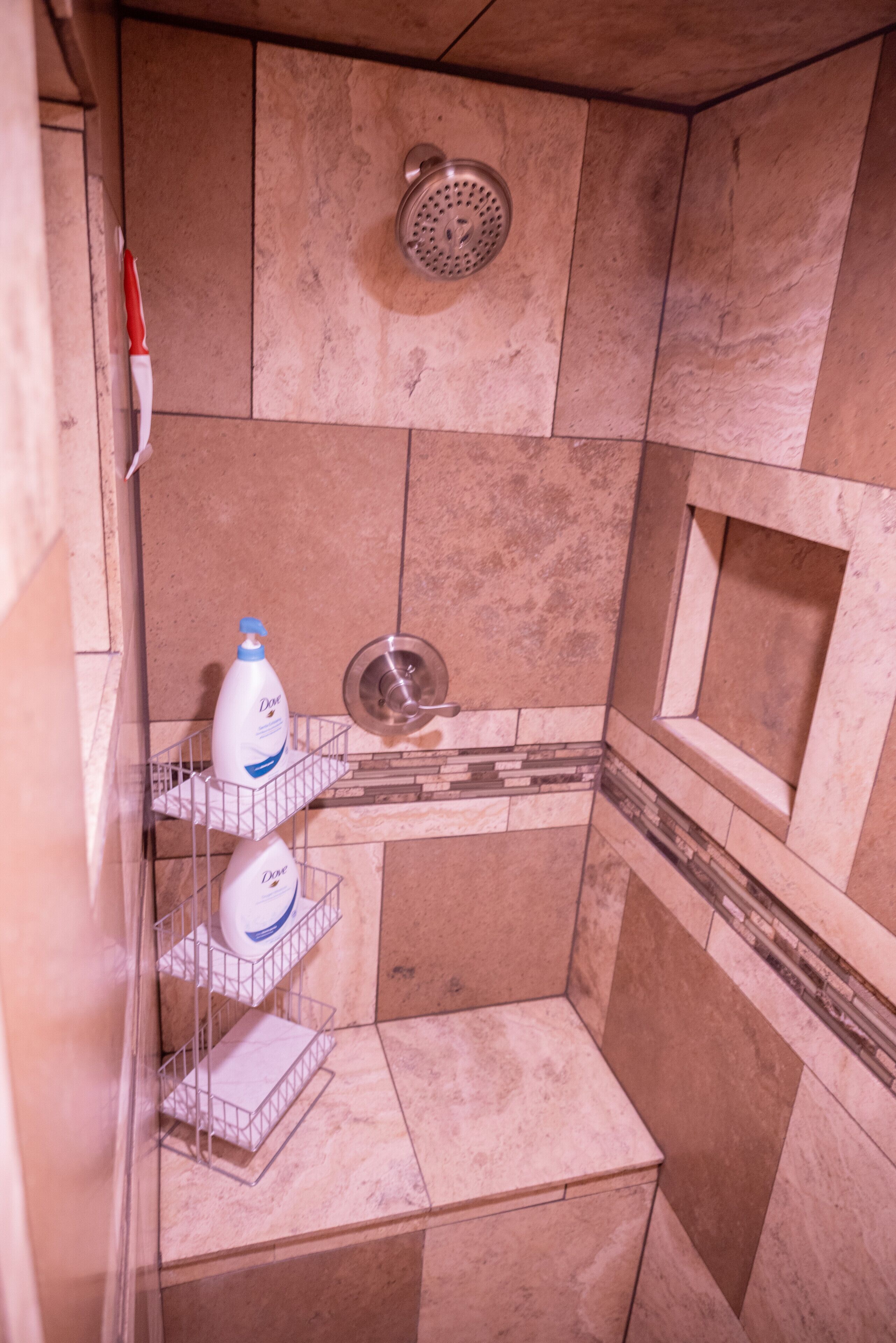 Ein Badezimmer mit Dusche, einem Handtrockner und einem Seifenspender auf einem Regal.