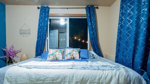 A bedroom with a bed, blue curtains, a window, and a wall decoration. - Home: Sleeps 4, Bedroom, Living, Bath, Office, Patio (Bothell)