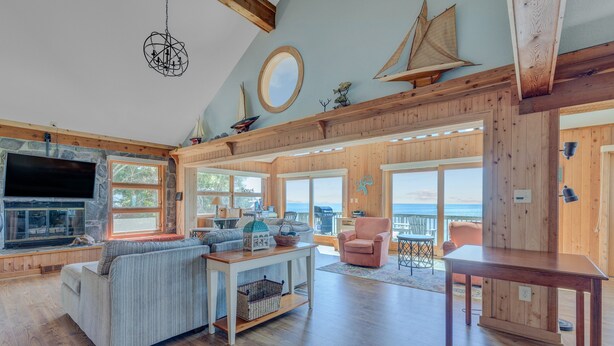 A spacious living room with a large TV, wooden furniture, and a view of the sea. - 7815-Tarhoo, | Soundfront Frisco Retreat | Pool & Sunset Views (Frisco)