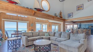 A spacious living area with a large sectional sofa, a round coffee table, and a view of the ocean. - 7815-Tarhoo, | Soundfront Frisco Retreat | Pool & Sunset Views (Frisco)