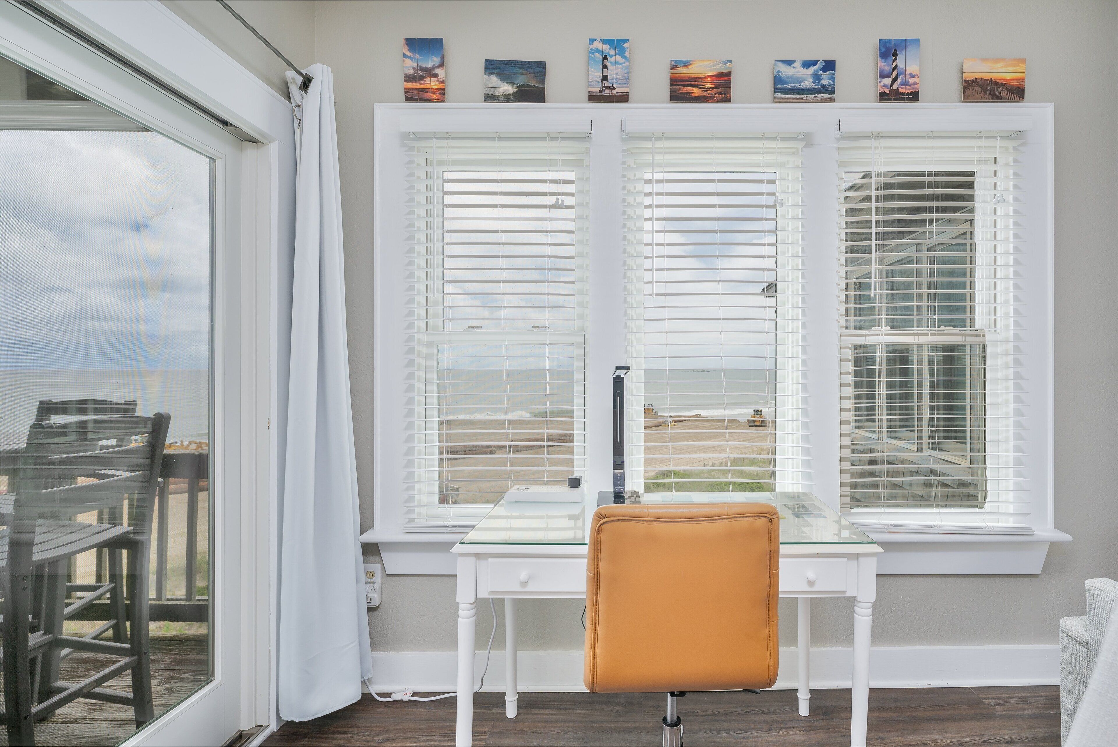 A room with a desk and chair, a window with blinds, and artwork on the wall.
