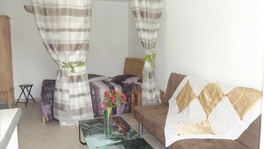 Ein Schlafzimmer mit einem Bett, einem Schlafsofa, einem kleinen Tisch mit Blumen und Vorhängen.