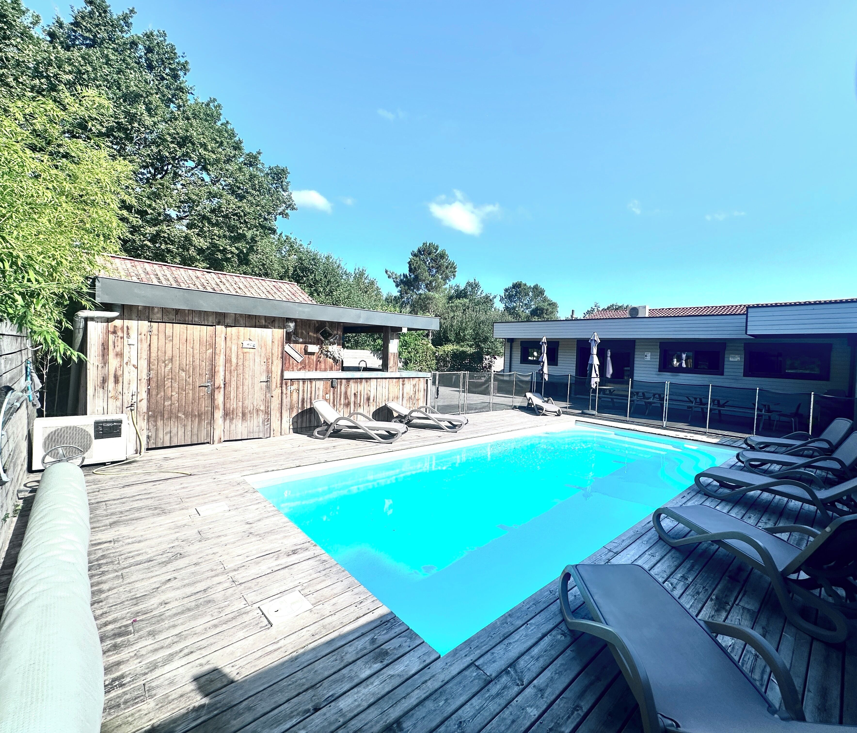 Ein Schwimmbad mit Liegestühlen, einer Holzterrasse und einem Gebäude mit einem Ziegeldach.