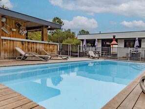 A swimming pool with lounge chairs, a wooden deck, and a building with a covered patio area.