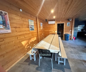 Een lange houten tafel met banken, een houten wand met posters en een prullenbak.
