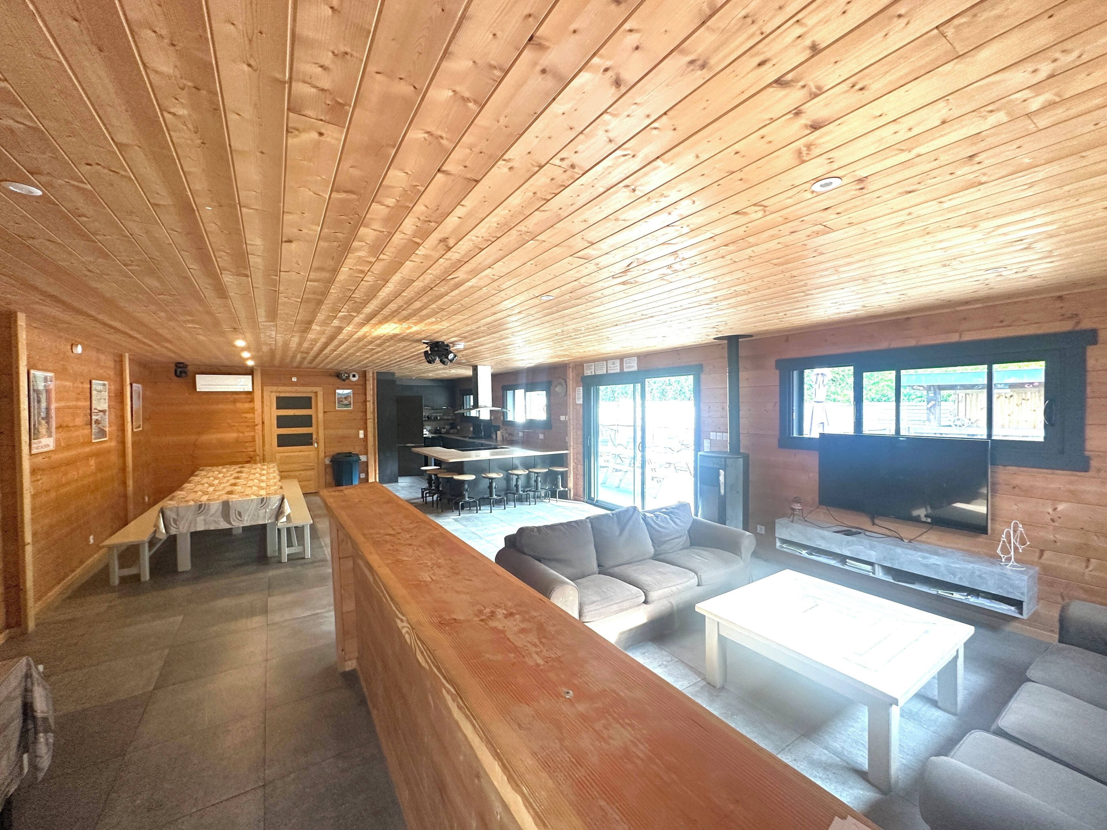 A wooden interior with a long bench, a sofa, a coffee table, and a television.