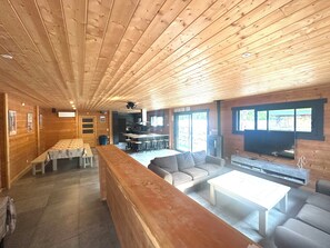 A wooden interior with a long bench, a sofa, a coffee table, and a television.