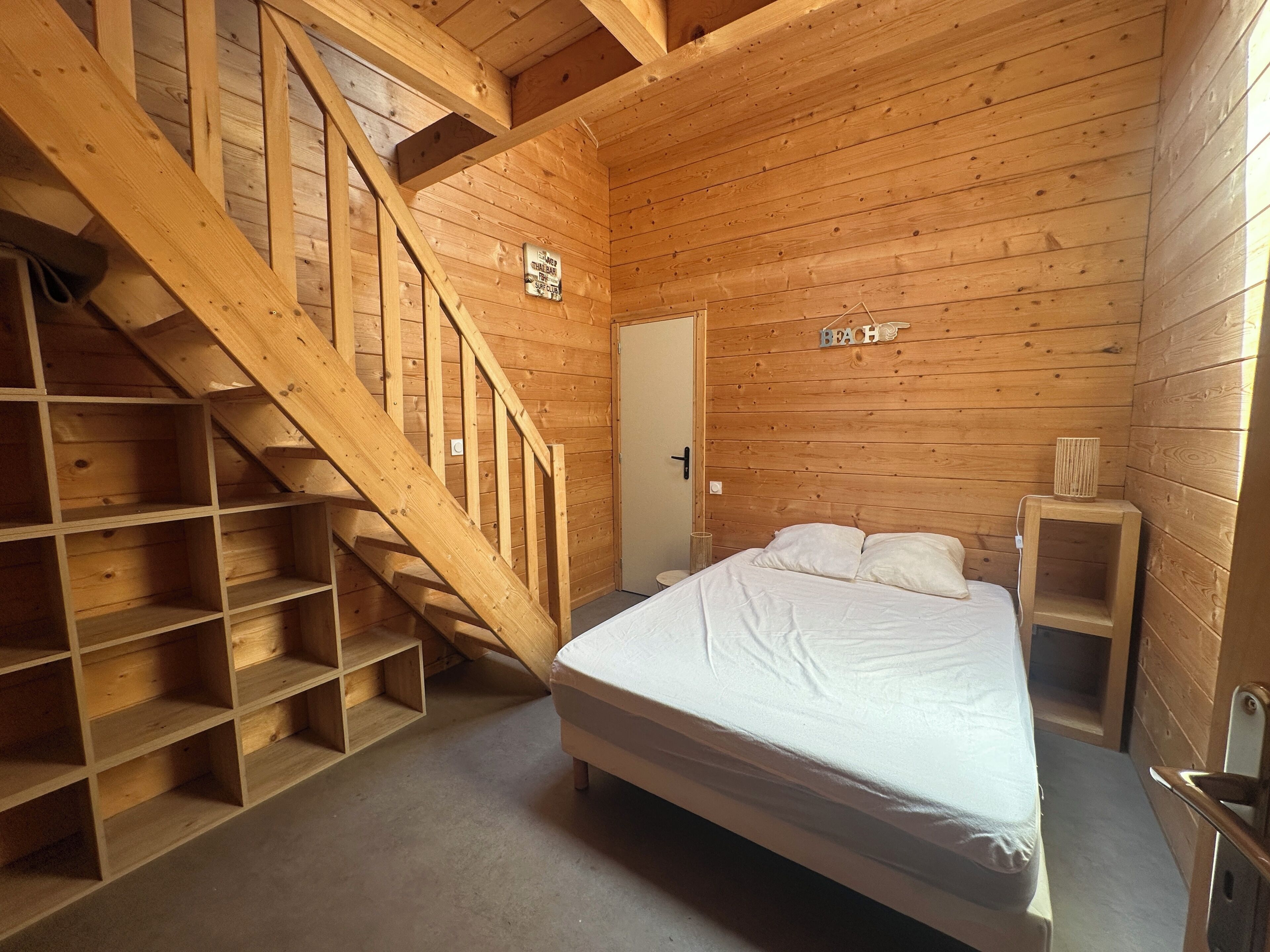 A wooden cabin bedroom with a bed, a wooden staircase, and a door.