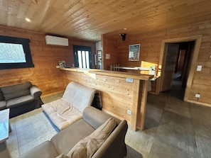 Een gezellig chaletinterieur met een houten plafond, een bank, een kleine tafel en een keukenhoek met een aanrecht.