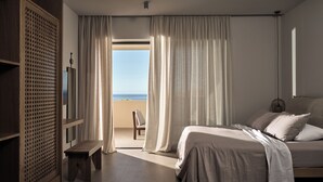 Un dormitorio con cama, un banco, un armario de madera y vistas al mar a través de las cortinas.