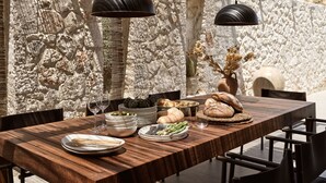 Une table à manger dressée avec des assiettes, des bols et du pain, le tout dans un décor de murs en pierre et de luminaires suspendus.