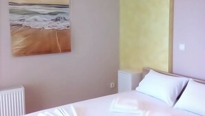 A bedroom with a bed, a white radiator, a painting of a beach scene, and a yellow accent wall. - Apartment in Rafina with Garden & BBQ (Rafina)