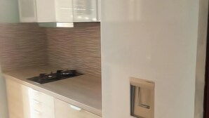 A kitchen with a modern design, featuring a stainless steel countertop, a built-in stove, and white cabinetry. - Apartment in Rafina with Garden & BBQ (Rafina)
