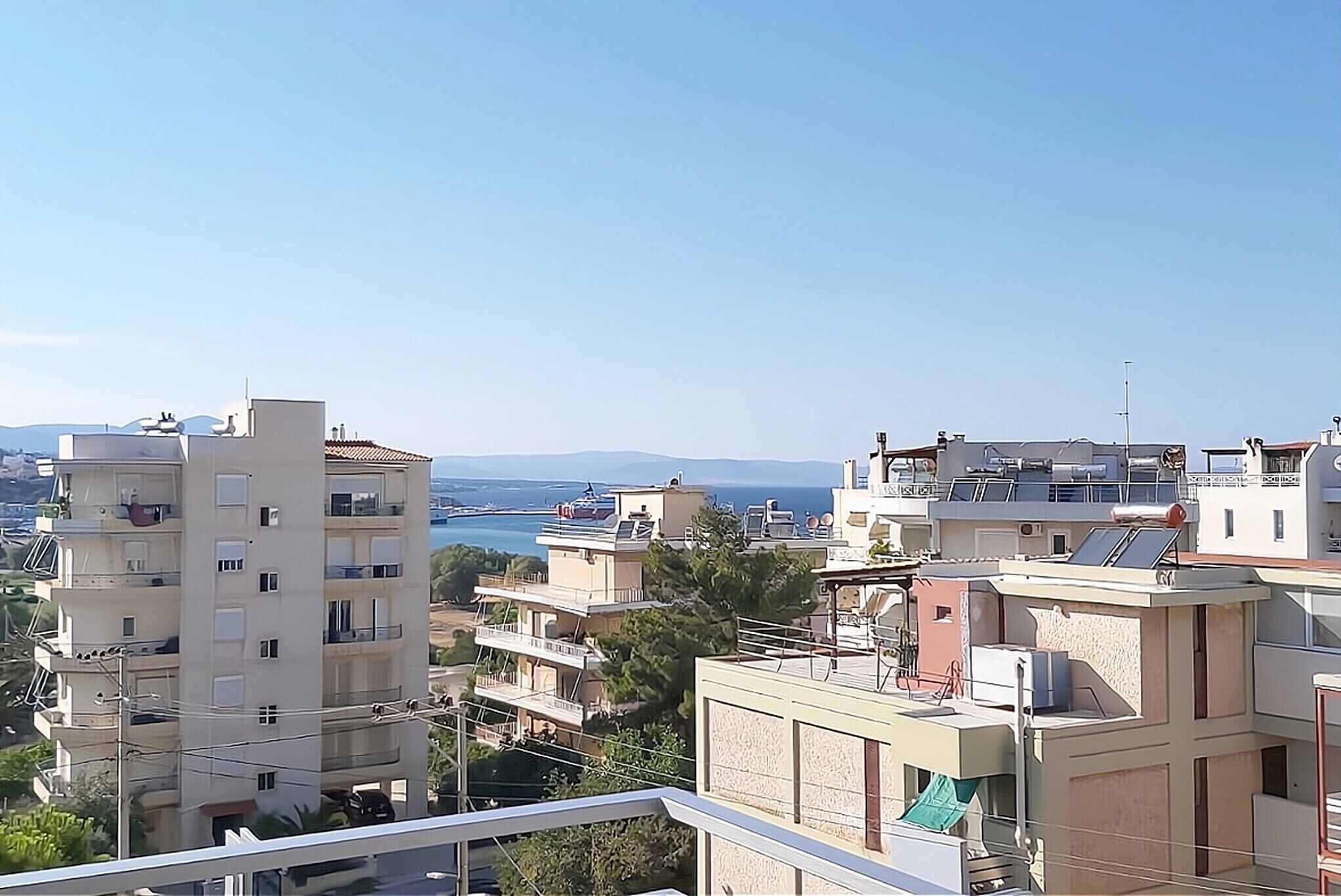 A residential area with multiple apartment buildings, some with balconies and solar panels, overlooking a body of water and distant mountains.