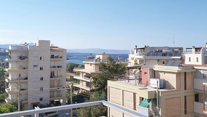 A residential area with multiple apartment buildings, some with balconies and solar panels, overlooking a body of water and distant mountains. - Apartment in Rafina with Garden & BBQ (Rafina)