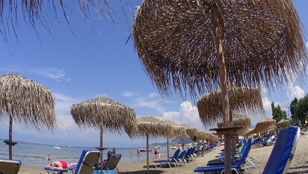 A beach with rows of blue lounge chairs and straw umbrellas. - Apartment in Mpenitses with Sea Views & Pool (Mpenitses)