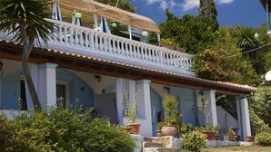 A two-story house with a balcony, surrounded by lush greenery and trees. - Apartment in Mpenitses with Sea Views & Pool (Mpenitses)