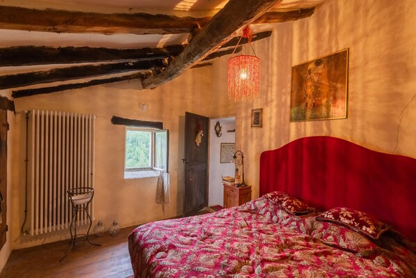 Un dormitorio con una cama tapizada en rojo, un radiador, una ventana y una araña.