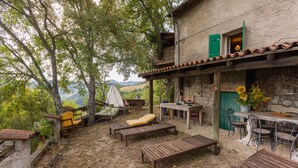 Un espacio al aire libre rústico con bancos de madera y una mesa, rodeado de vegetación y vistas al campo.