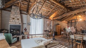 Una habitación acogedora y rústica con chimenea de piedra, vigas de madera, una cama con ropa de cama a rayas y un comedor con muebles de madera.